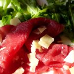Bresaola appoggiata su un tagliere con erbe aromatiche e fette di limone.